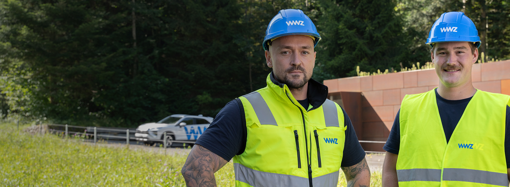 Zwei Mitarbeiter mit Helm und Leuchtweste blicken in Kamera.