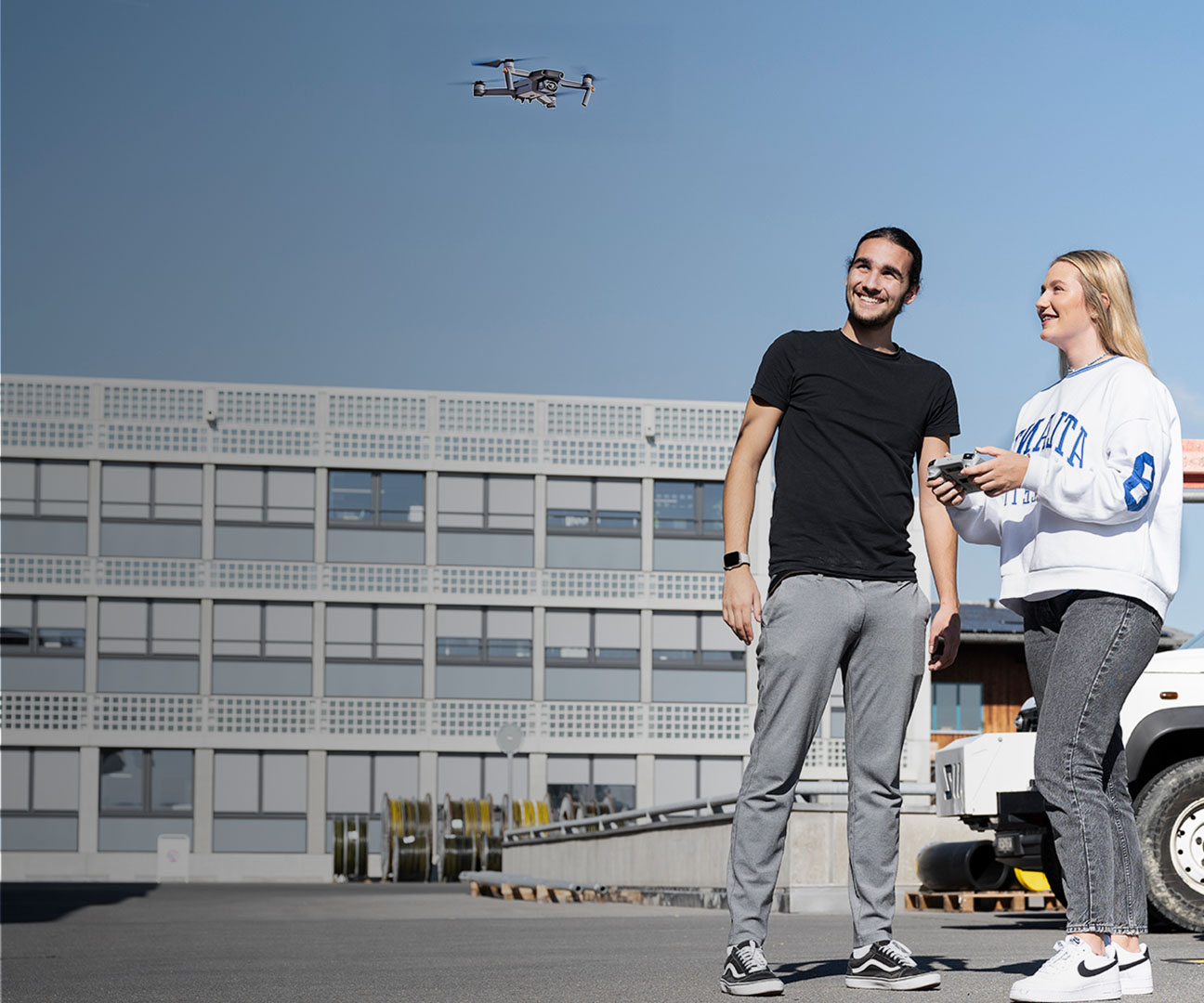 Zwei Lernende steuern eine Drohne bei sonnigem Wetter.