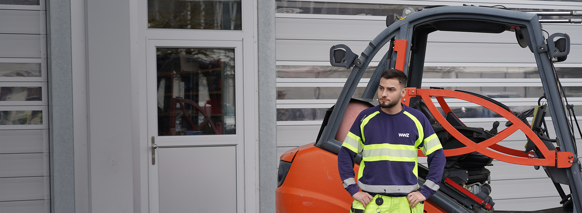 Logistiker in WWZ-Arbeitskleidung steht vor Gabelstapler