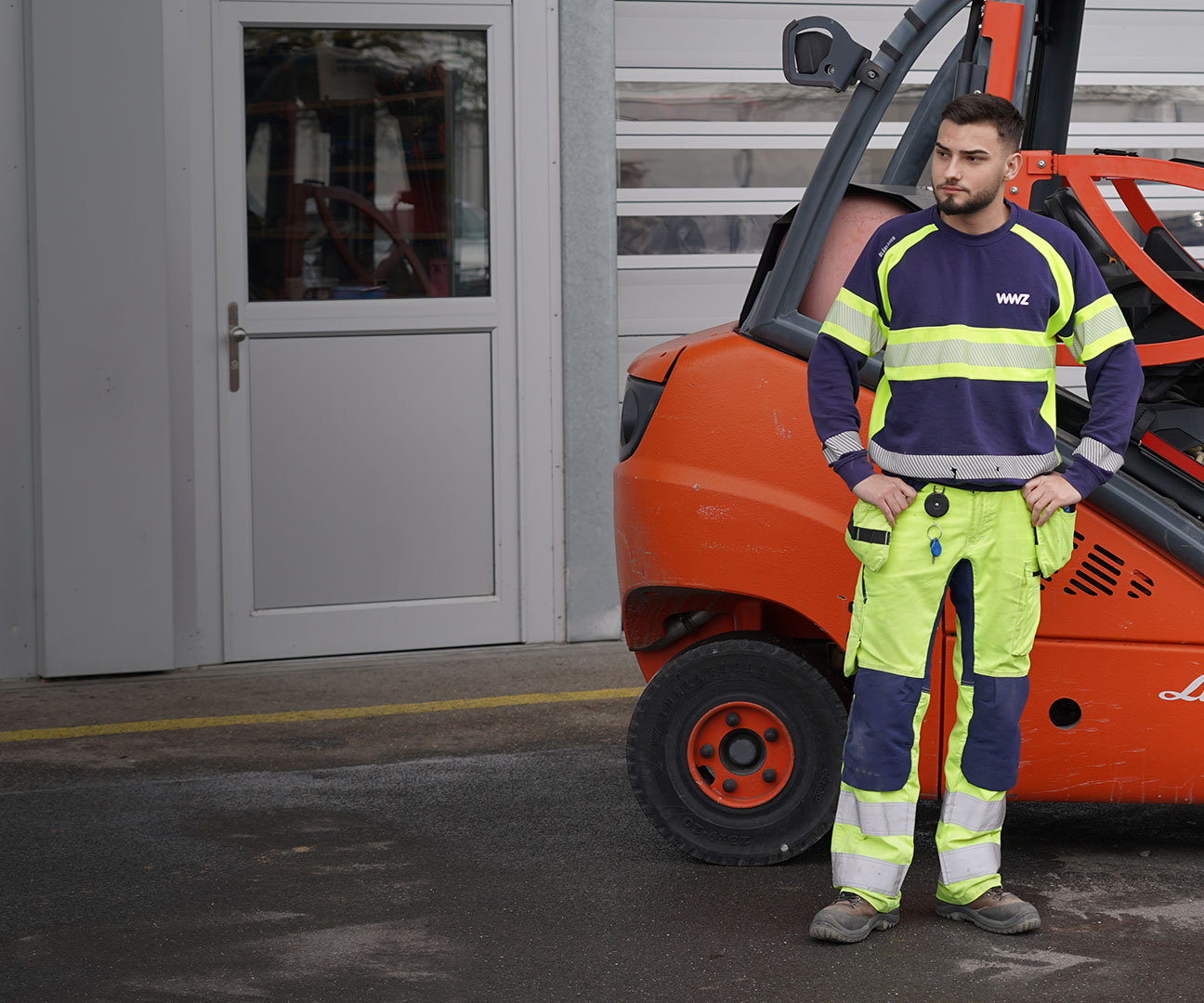 Logistiker steht vor rotem Gabelstapler in Arbeitskleidung