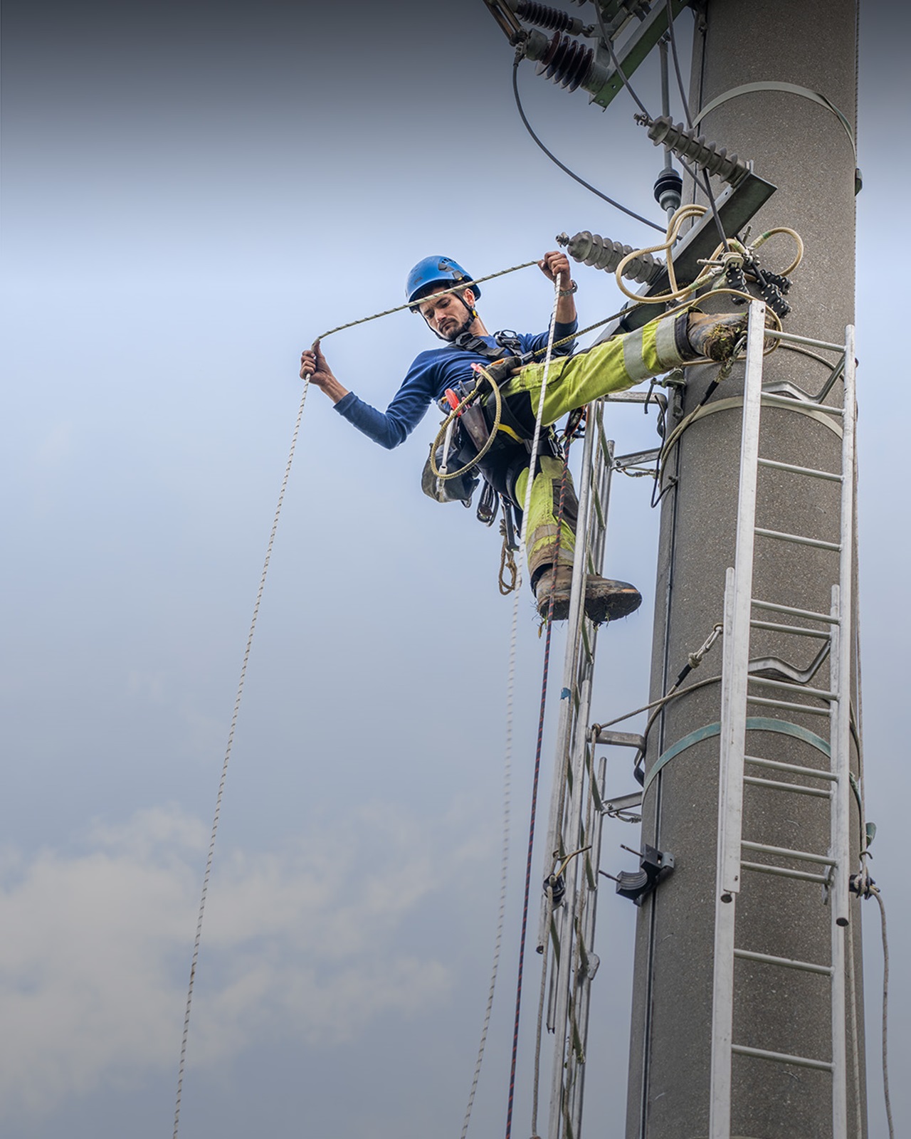 Netzelektiker hängt an Strommast und schaut in die Tiefe.