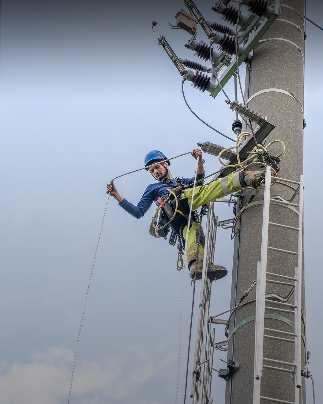 Netzelektiker hängt an Strommast und schaut in die Tiefe. 