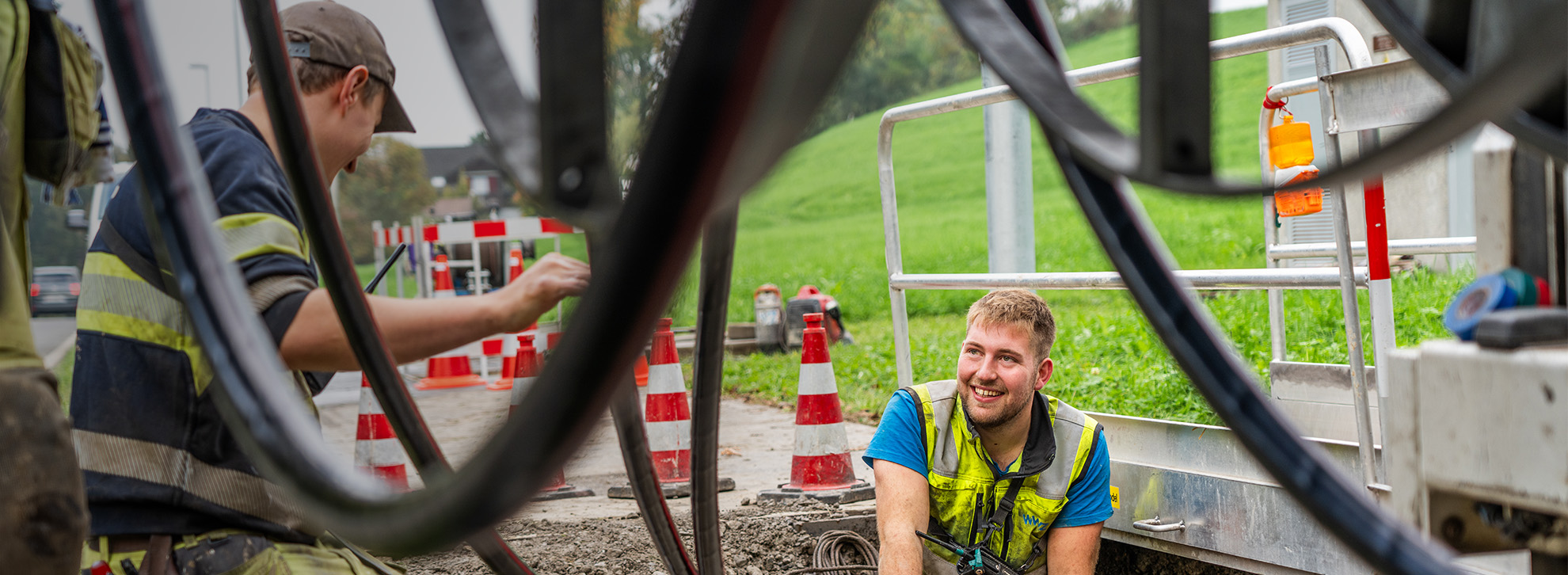 Zwei junge WWZ-Mitarbeiter tätigen Stromarbeiten an Strasse.