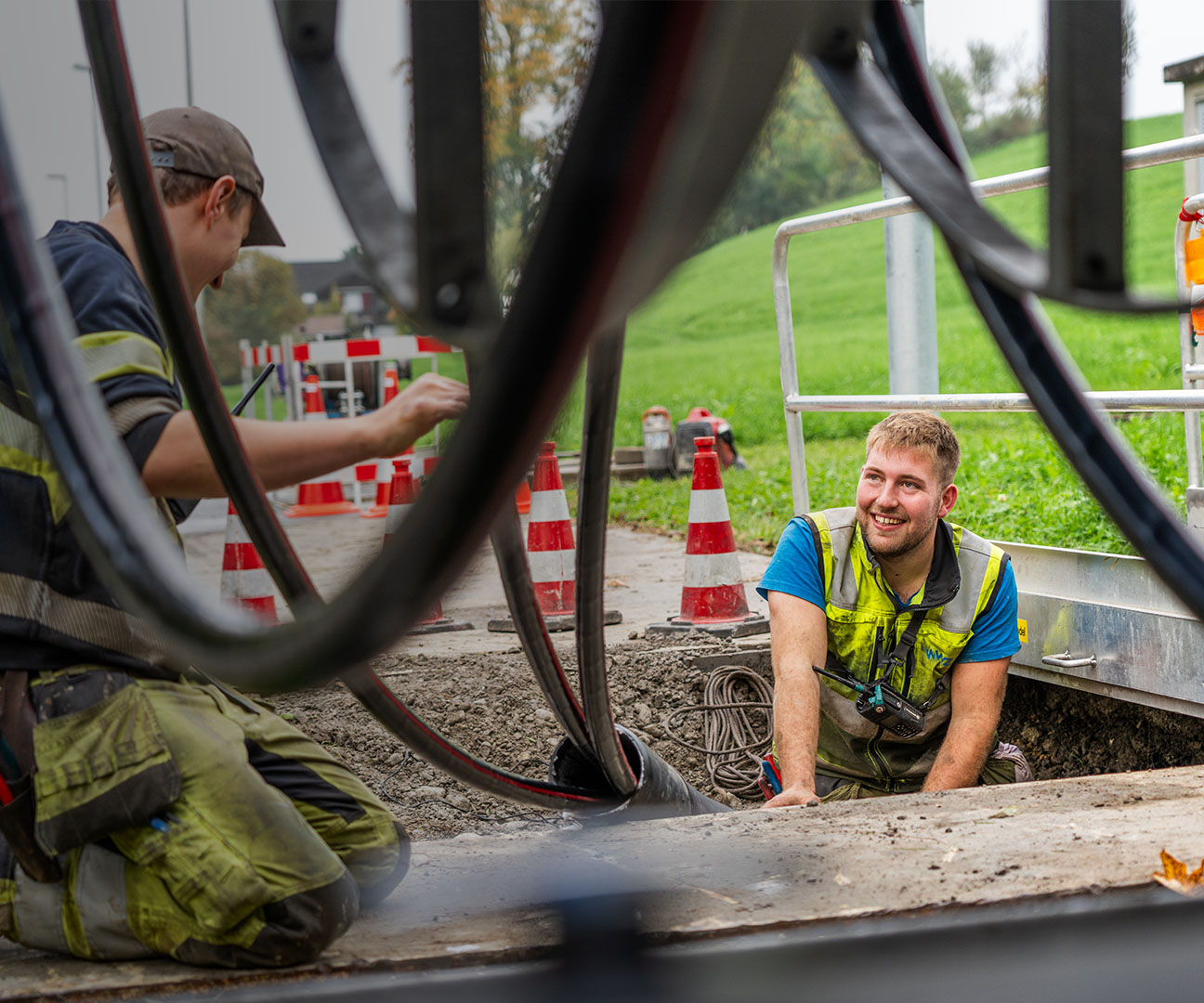 Zwei junge WWZ-Mitarbeiter tätigen Stromarbeiten an Strasse.  