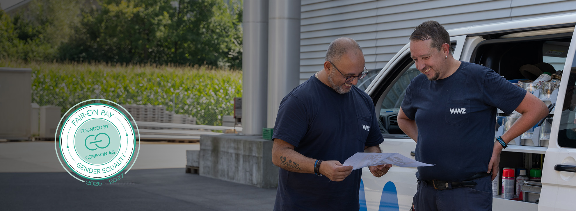 Zwei Männer stehen vor WWZ-Auto und schauen sich einen Plan an. 