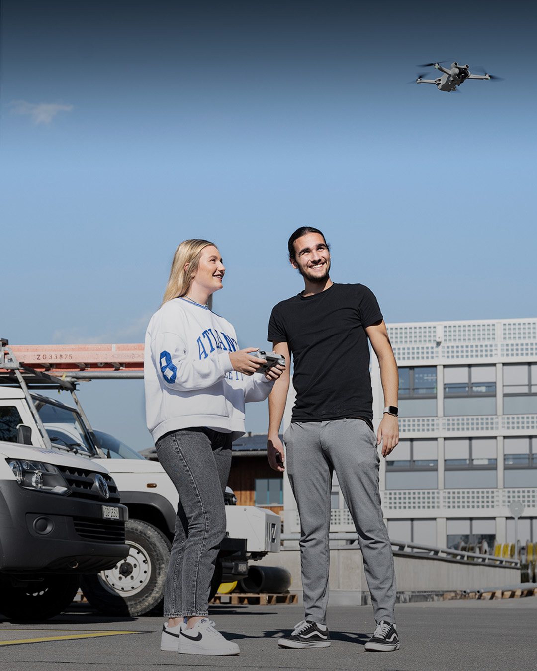 Junger Mann und Frau fliegen eine Drohne vor einem Gebäude. 