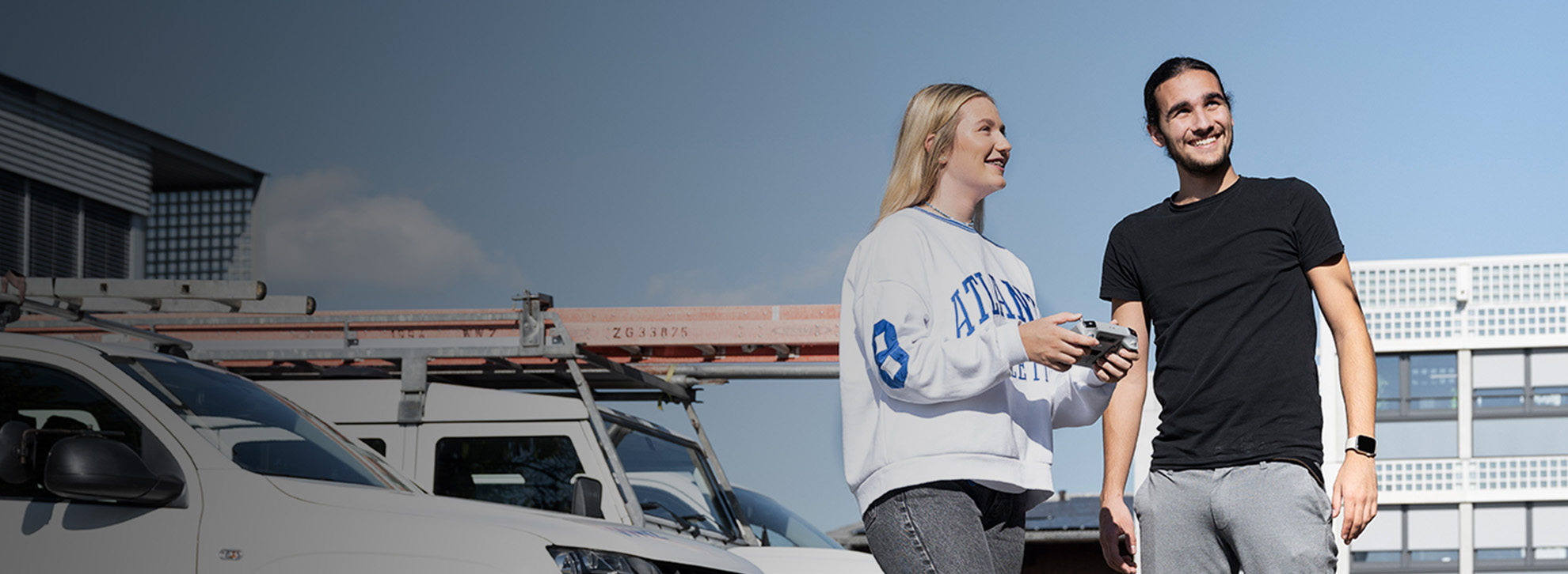 Junger Mann und Frau fliegen eine Drohne vor einem Gebäude. 