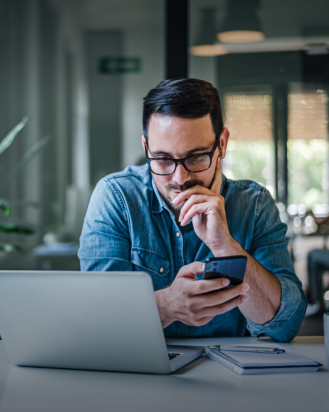 Mann an Laptop mit Mobiltelefon in der Hand. 