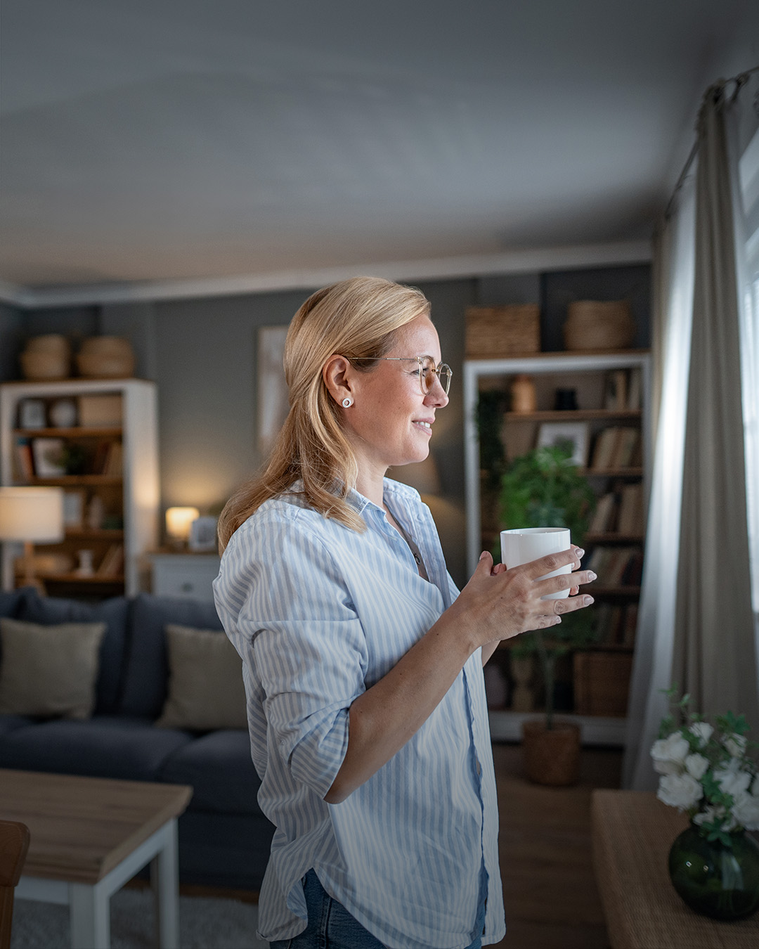 Frau in modernem Wohnzimmer schaut aus dem Fenster. 