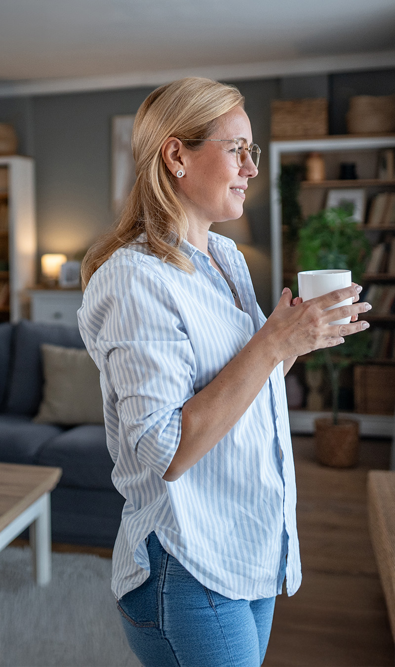 Frau in modernem Wohnzimmer schaut aus dem Fenster. 