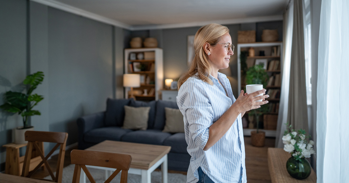 Frau in modernem Wohnzimmer schaut aus dem Fenster. 