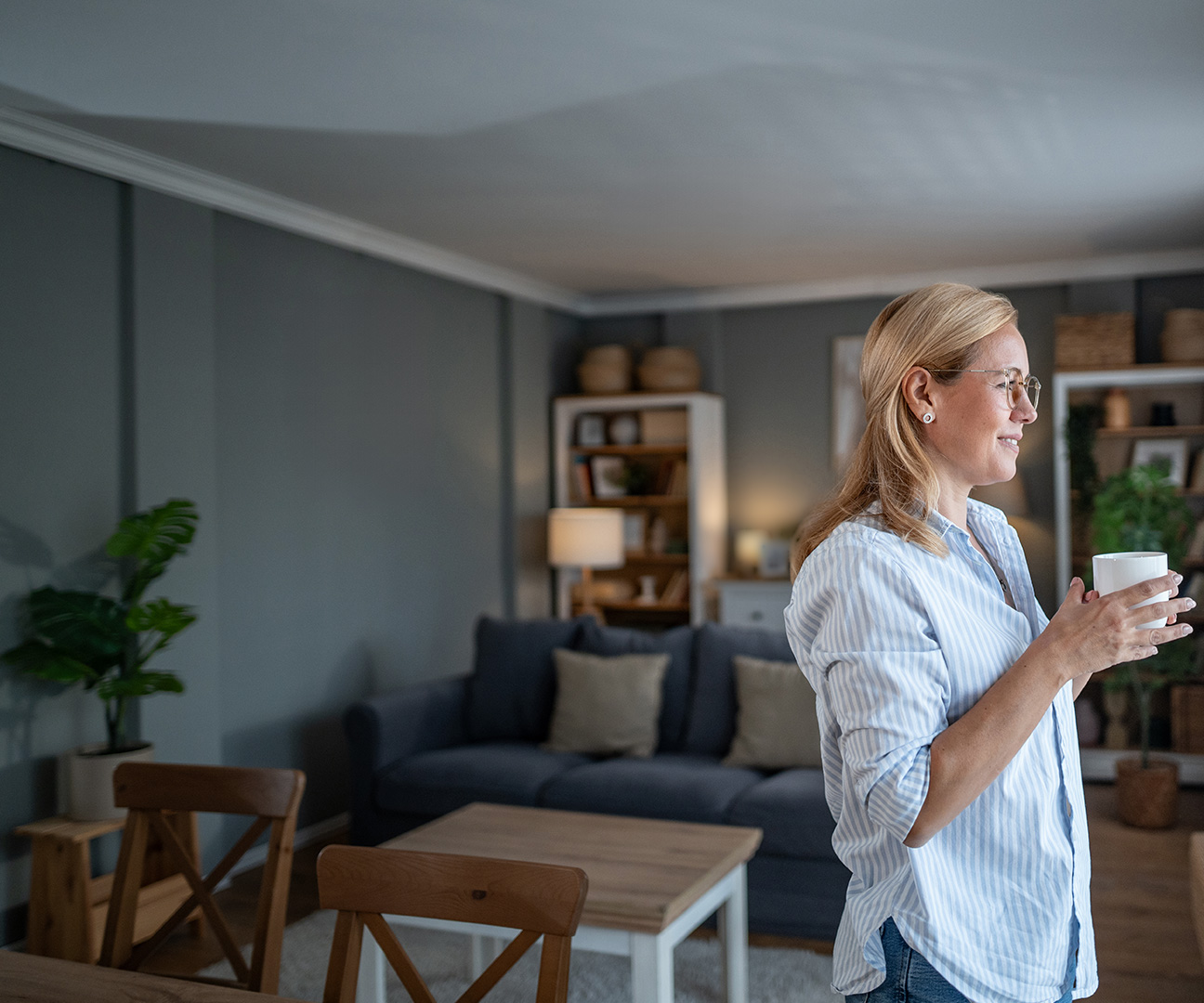 Frau in modernem Wohnzimmer schaut aus dem Fenster. 