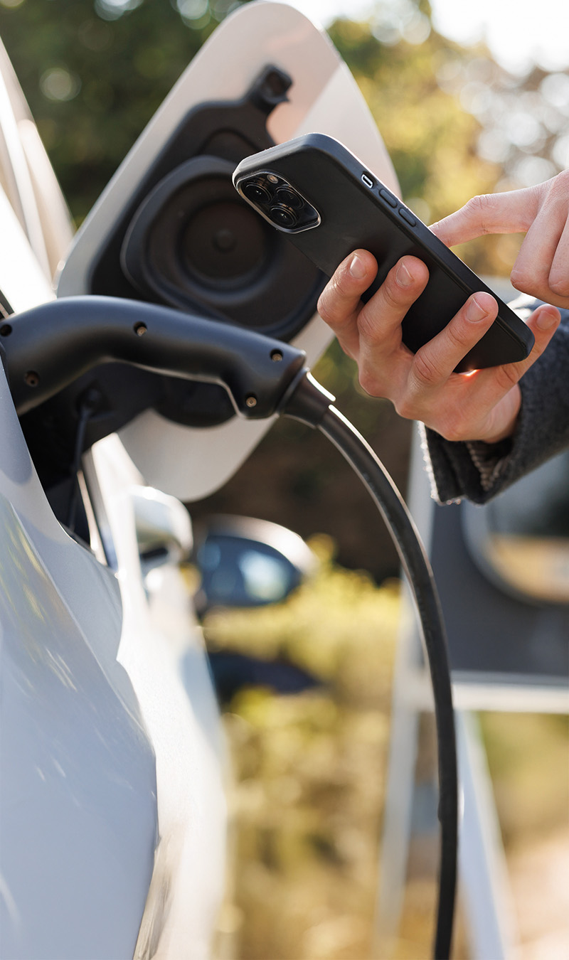 Mann mit Mobiltelefon lädt E-Auto
